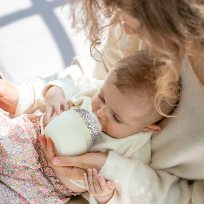 Baby being held by a person, holding a bottle