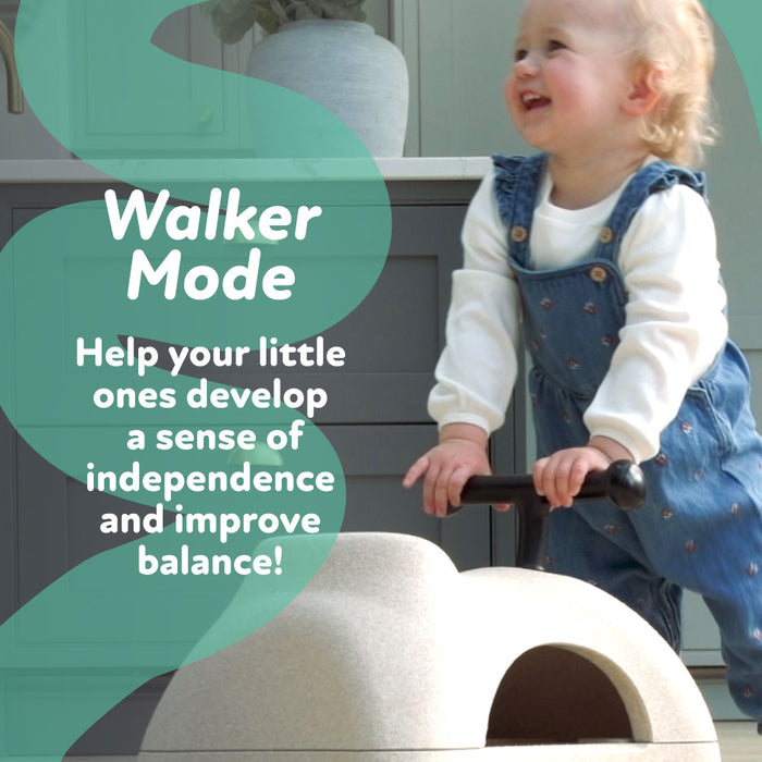 A smiling toddler in blue overalls stands in a bright kitchen, holding the Boogie Buggy | Pink. Text reads: Walker Mode. Support independence and balance with this 3-in-1 scooter featuring soft EPP foam!.