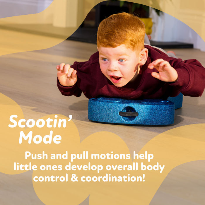 A young red-haired child lies on their stomach on a sage Boogie Buggy scooter board, moving forward with arms extended. Text reads: Scootin’ Mode. Push and pull motions help kids build body control & coordination!.