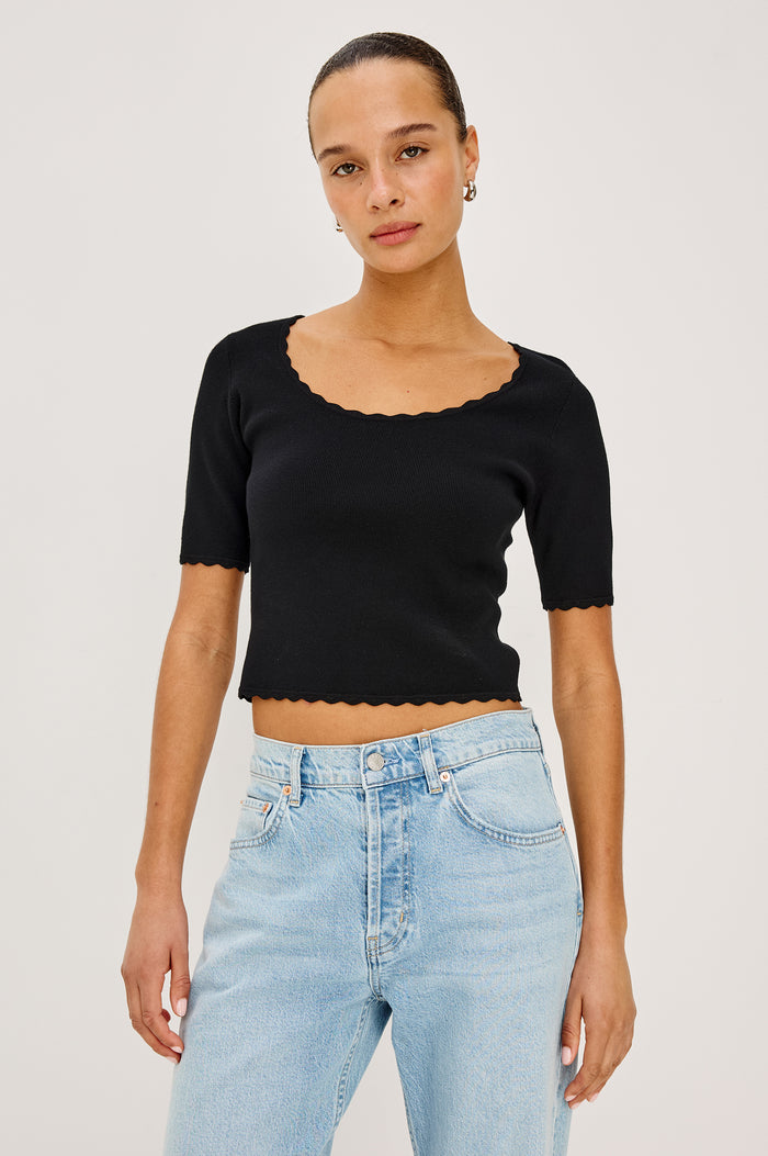 Louanna Fitted Cropped Top in Compact Knit With Scallop-Trimmed Scoop Neckline, Short Sleeves, and Hem in Black Colorway - Upper Body Front View Featured on Model