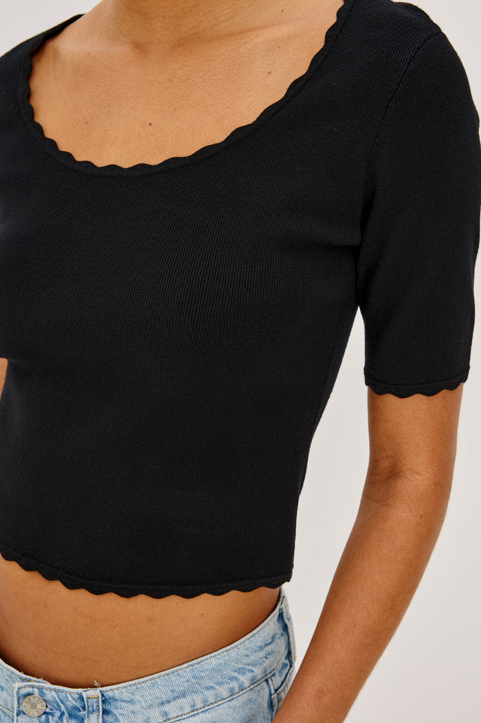 Louanna Fitted Cropped Top in Compact Knit With Scallop-Trimmed Scoop Neckline, Short Sleeves, and Hem in Black Colorway - Upper Body Close Up Front View Featured on Model