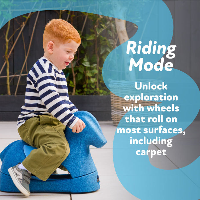 A young child with red hair, in a striped shirt and green pants, rides the Rock 'N Ride | Sage. Text reads: Riding Mode – Unlock exploration with wheels that roll on most surfaces, including carpet.